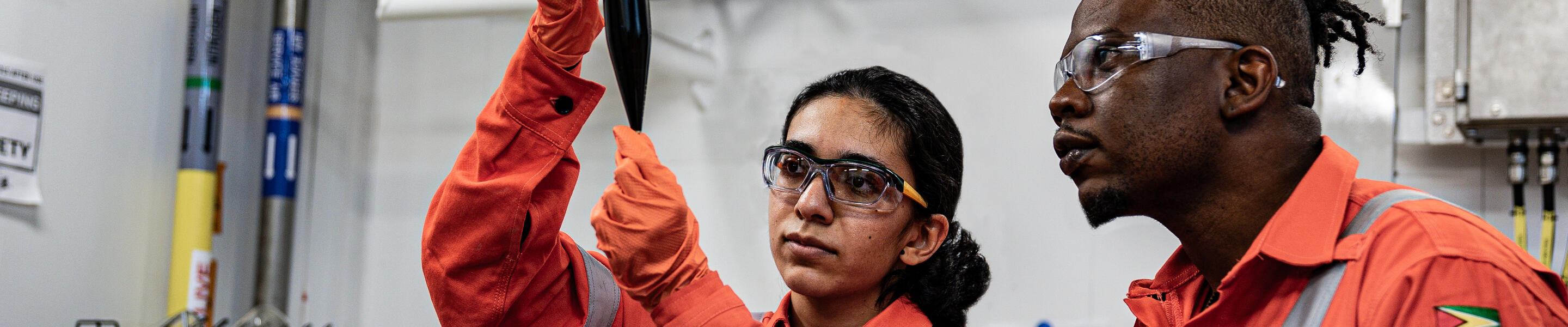 Woman and man looking at a tube wearing ExxonMobil Guyana safety uniforms