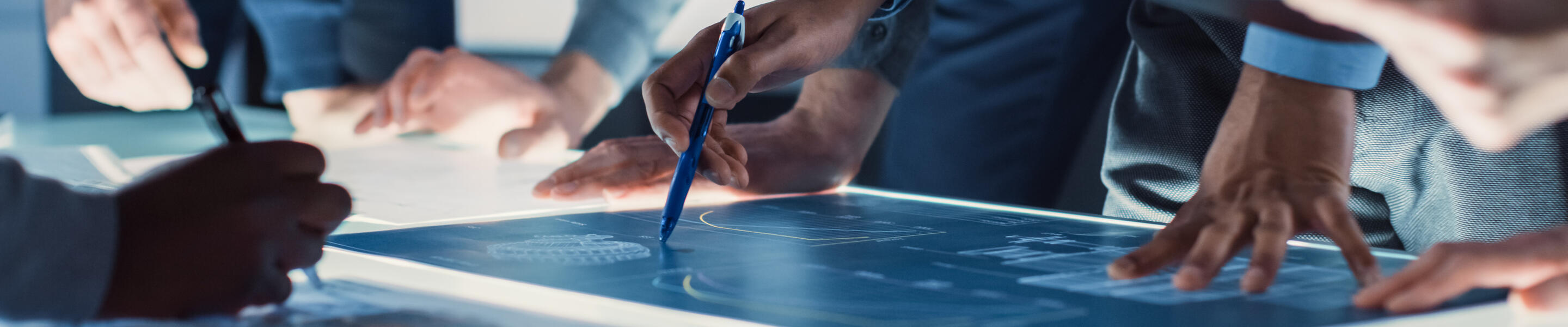 illuminated table-top showing digital drawings, people's hands, one holding a tablet and another a pen/stylus