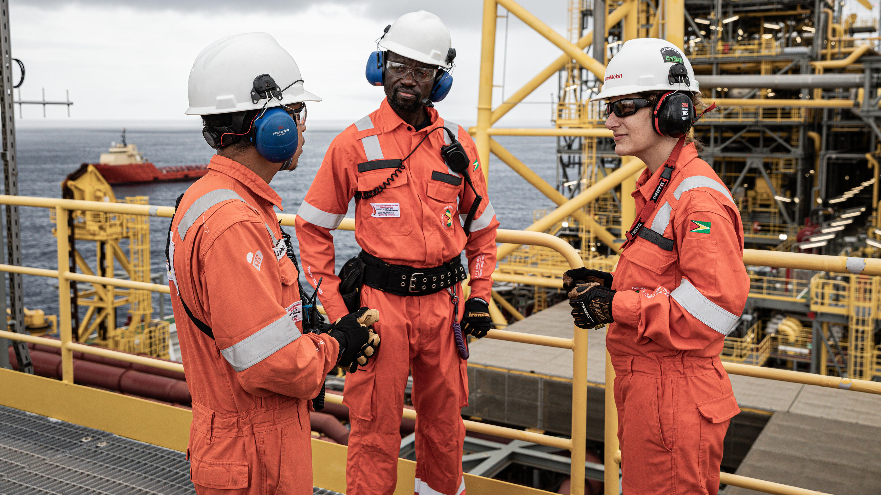 Three employees in hard hats talking on a vessel with the ocean in the background