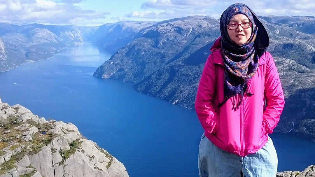 A women standing in Norway with water and mountains in the background.
