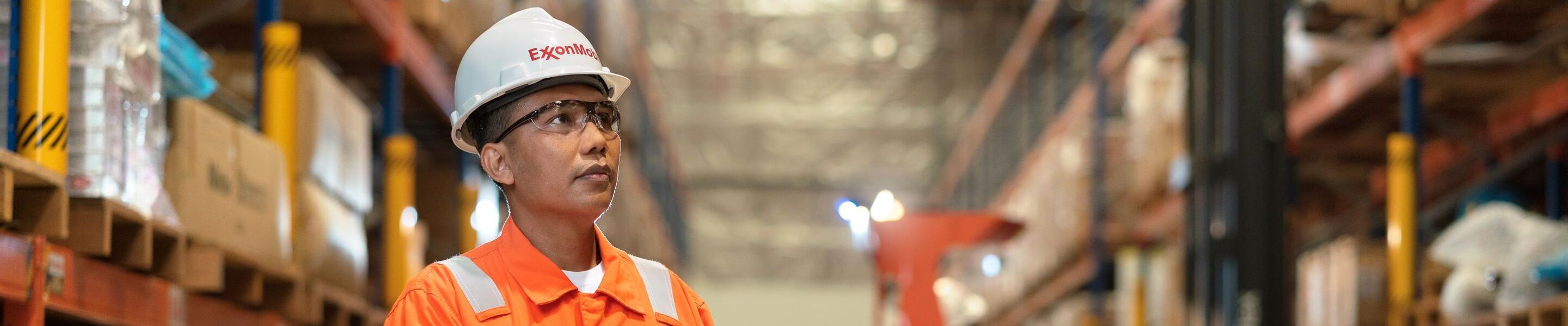 A person in an orange safety jumpsuit and a white hard hat labeled 