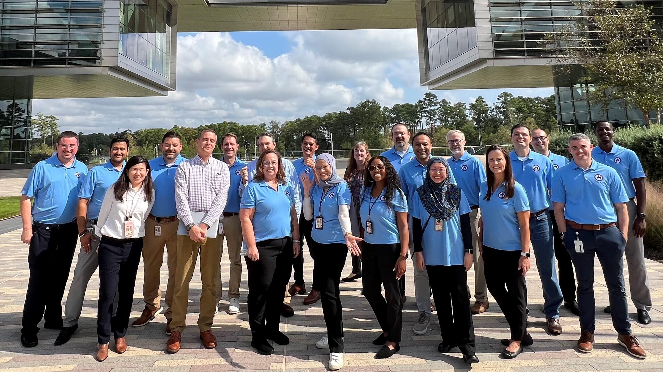group of ExxonMobil employees mostly wearing blue shirts and standing in front of Houston campus building on sunny day