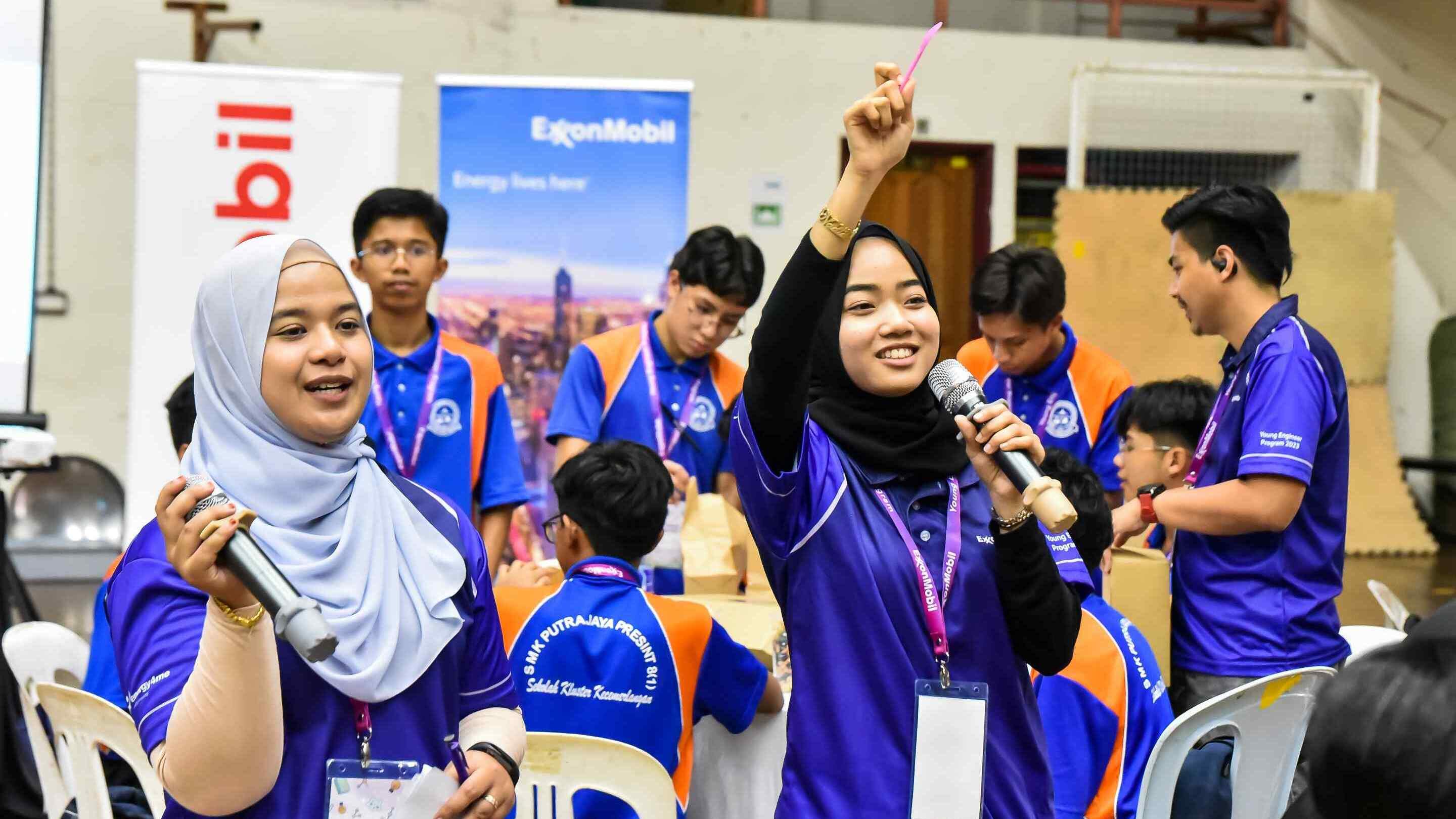 ExxonMobil Malaysia employees holding microphones while volunteering at student event.