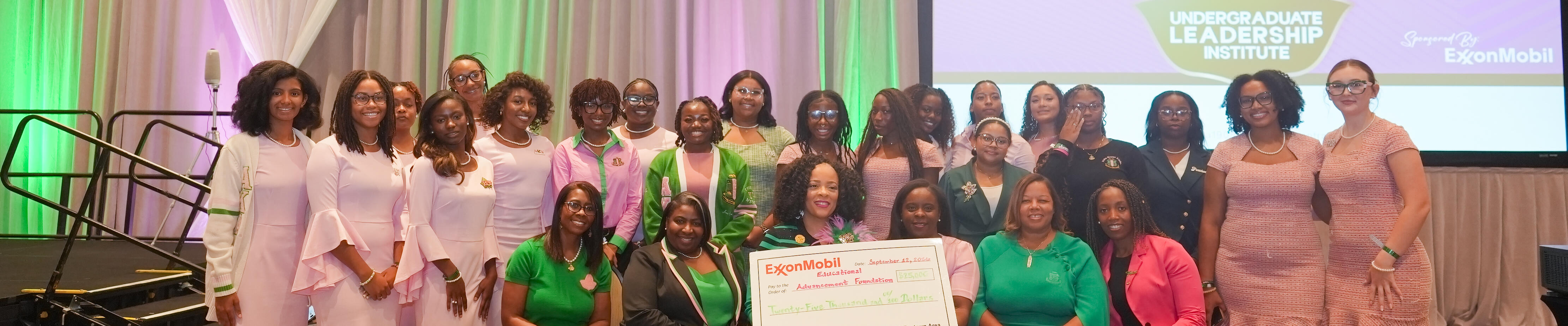 A large group of women pose together in a ballroom, many wearing coordinated pink and green outfits.