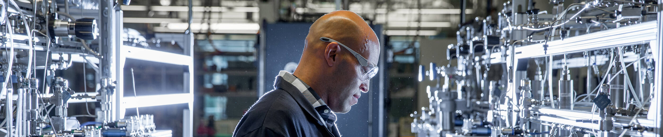 Worker in a lab wearing a black uniform and safety gear reading a notebook.