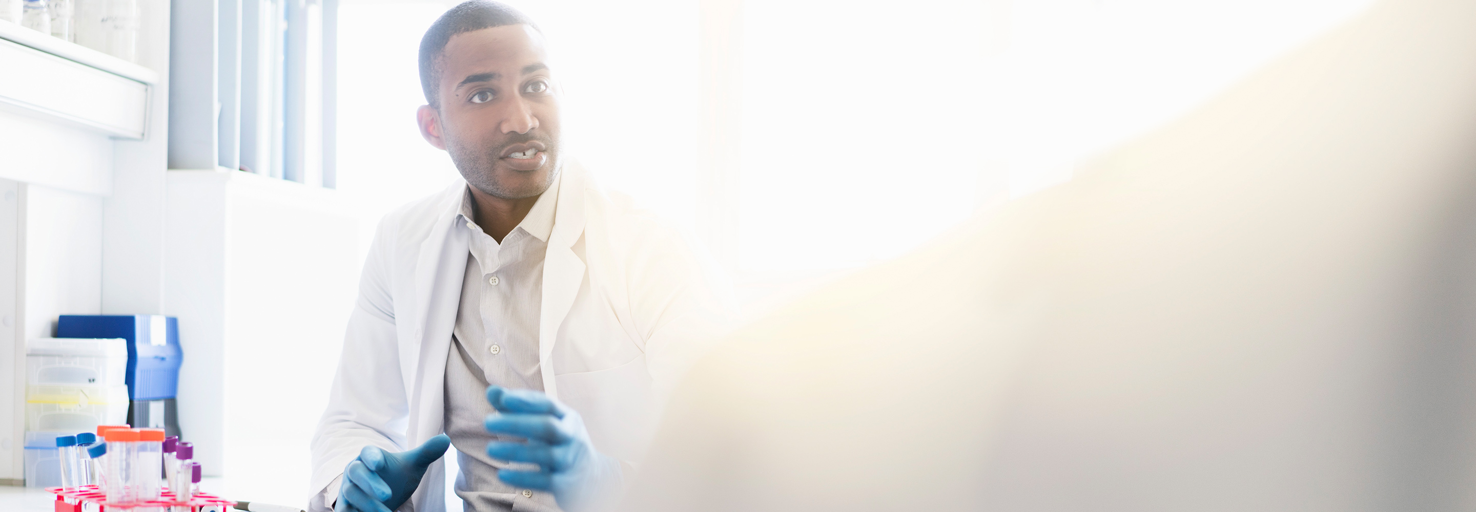 A male scientist sitting at a workspace with test tubes.