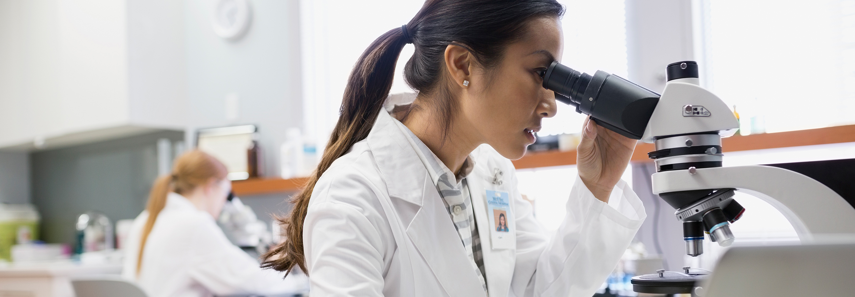 Two female scientists in their lab, both looking into microscopes.